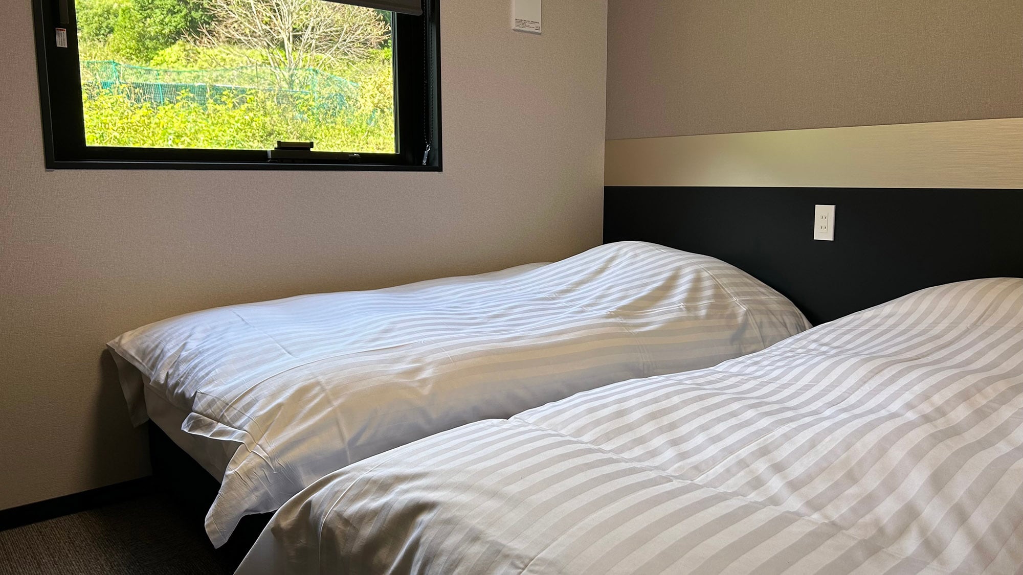 ・[Twin Room] A bright room with a large window. The outlet next to the bed is perfect for charging.