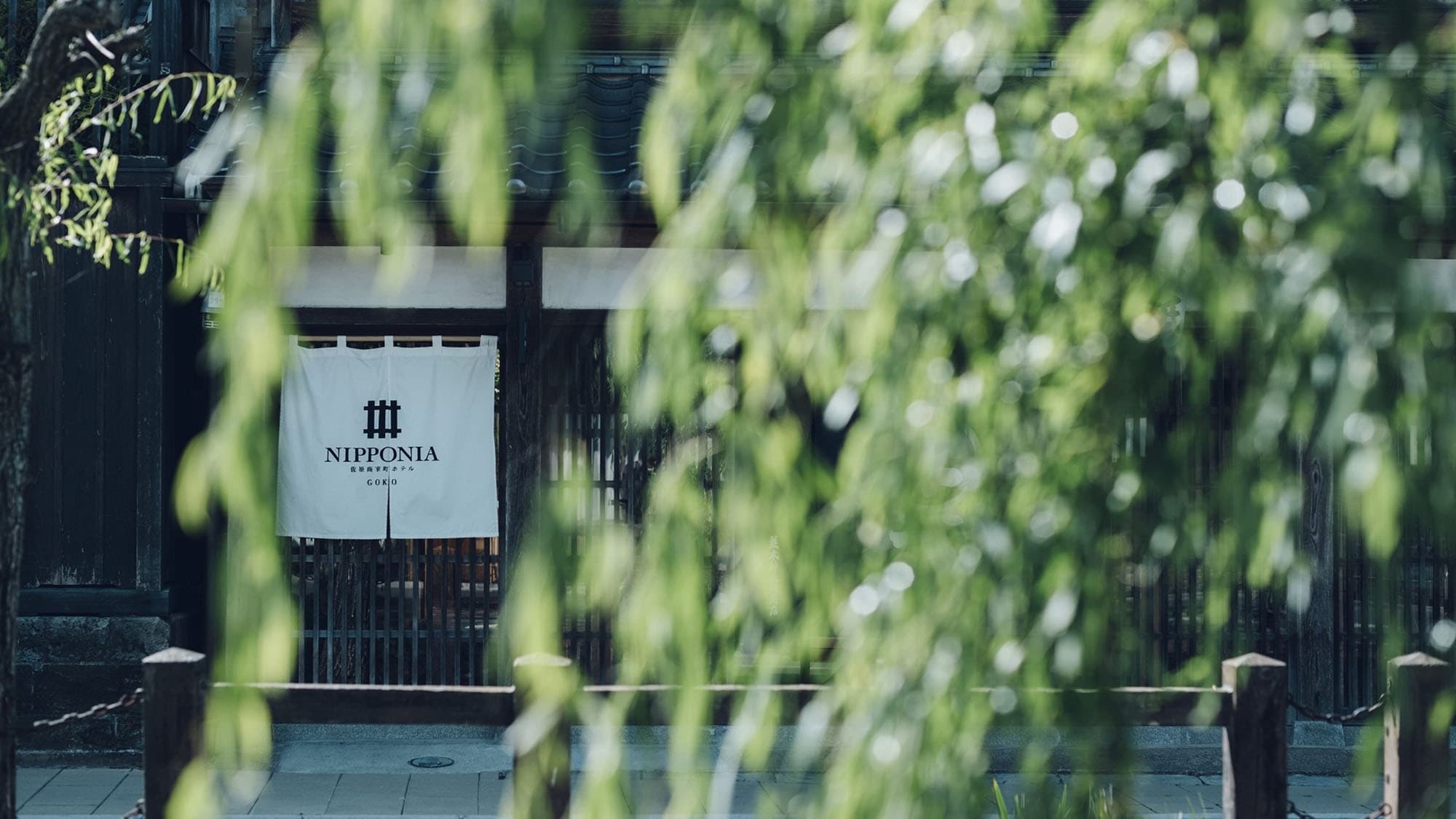 [Exterior] The accommodation building appears as you walk along, soothed by the greenery of the willow trees.