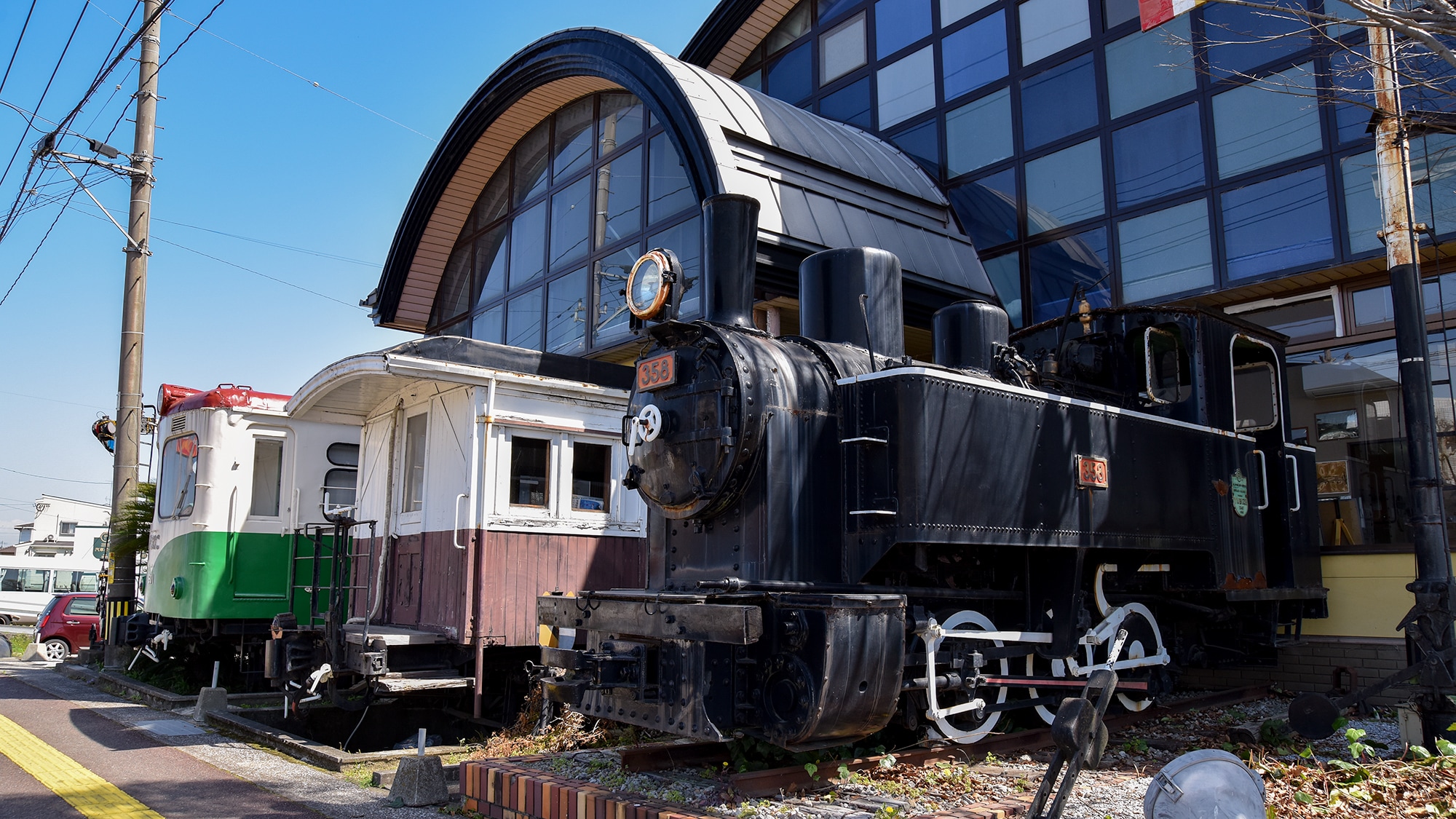 *[Exterior of the main dining hall] Steam locomotives, wooden passenger cars, and diesel railcars are lined up.