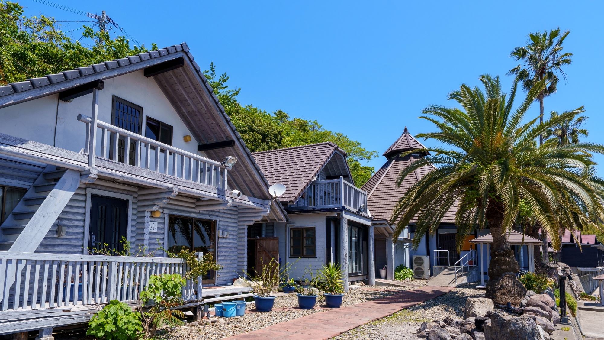 [Cottage Exterior] A seaside cottage with a pleasant sea breeze and swaying palm trees.