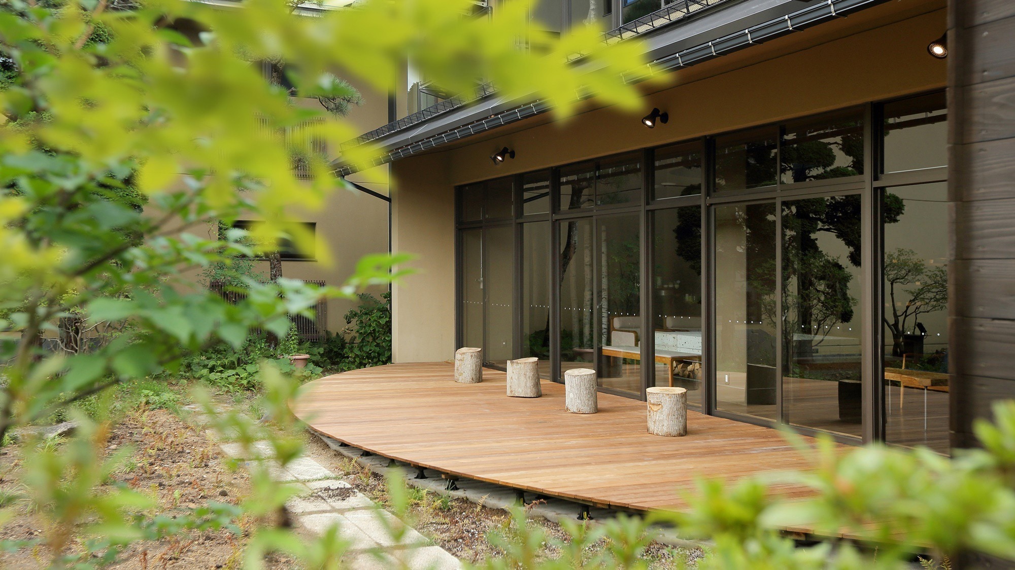 [Courtyard] There are fern plants and birch trees spreading in front of the wooden deck. Will be lit up at night
