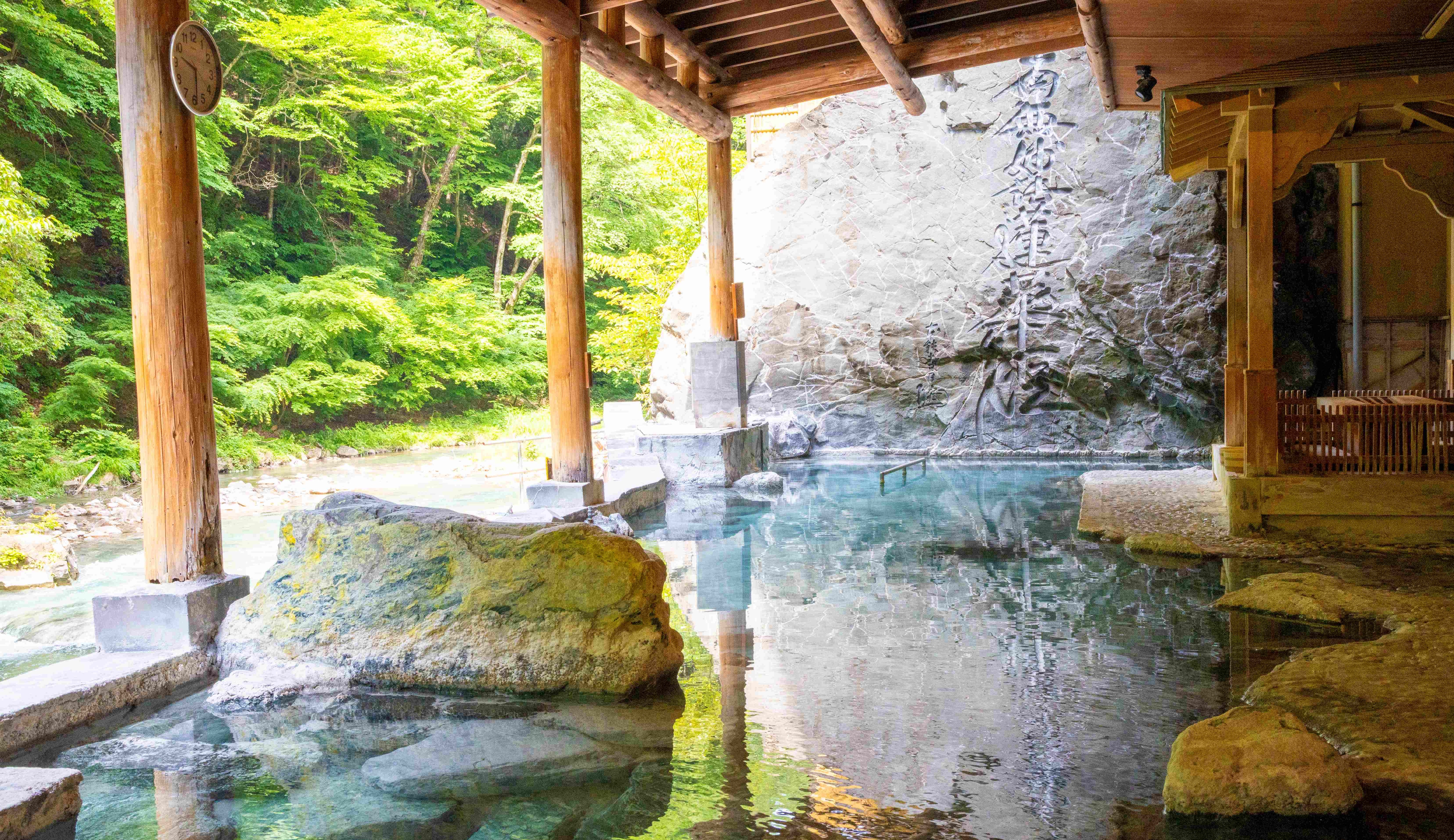 [Open-air bath with Buddhist mantra inscribed on it] Facing the Shimagawa River, the bath is 30 meters long and offers a fantastic sense of openness. The large rock inscribed with the Buddhist mantra is a striking feature.