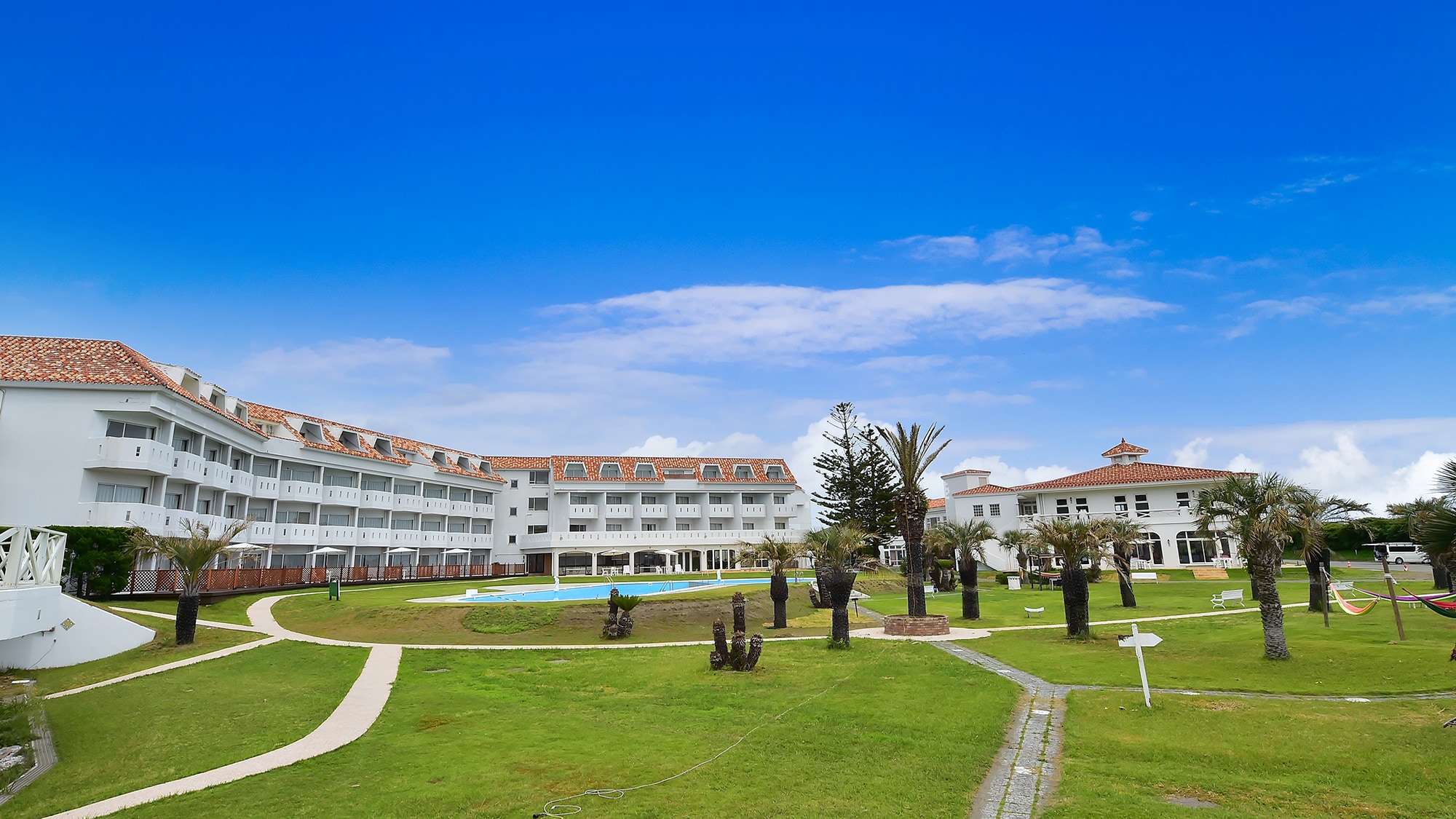 一座白色的酒店建筑围绕着一个大花园。中心有一个游泳池。