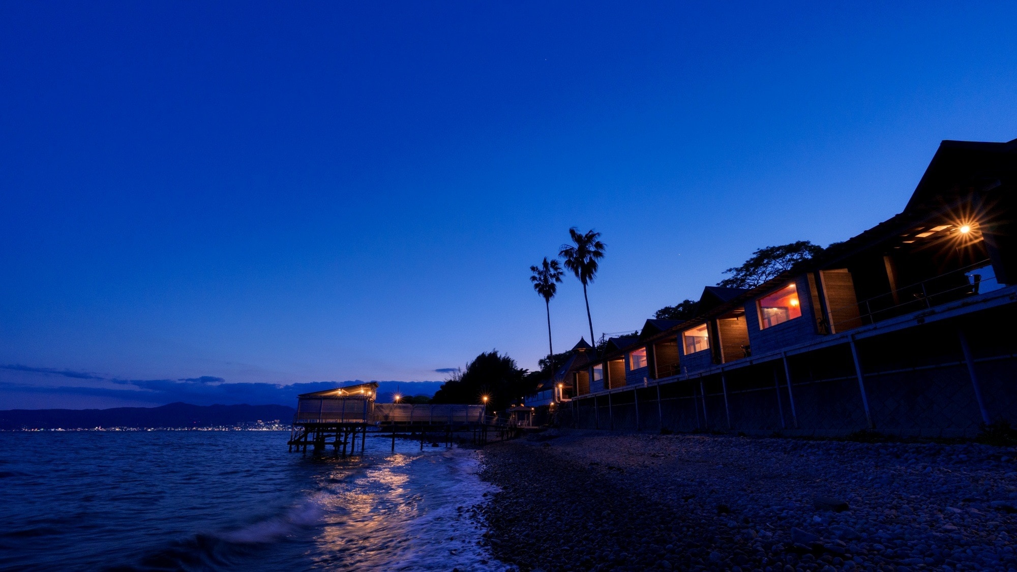 [Lodge exterior] The gentle sound of waves echoes along the coastline at night, enveloped in a magical blue hour.