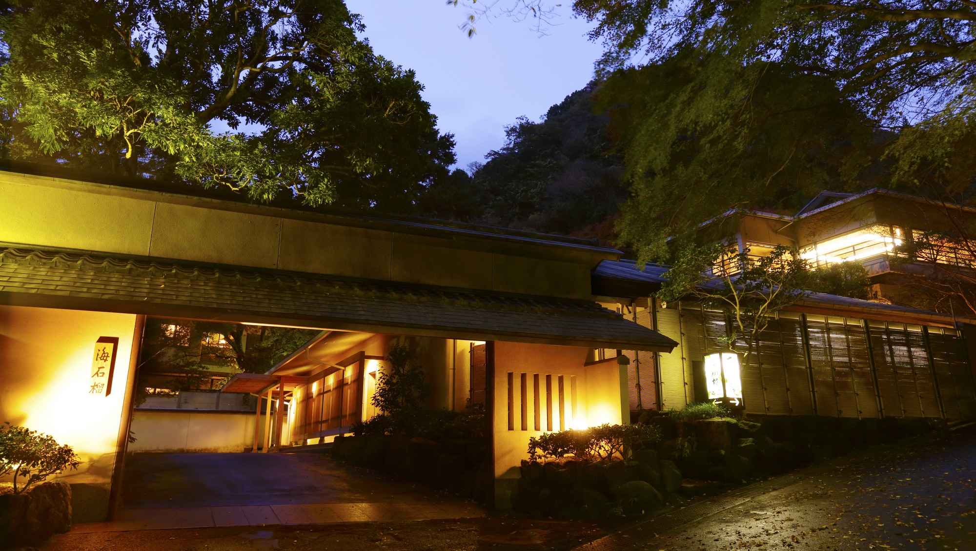 [Exterior] The main gate of the building at dusk. The contrast between the blue of the mountains and the brightness of the entrance is beautiful.