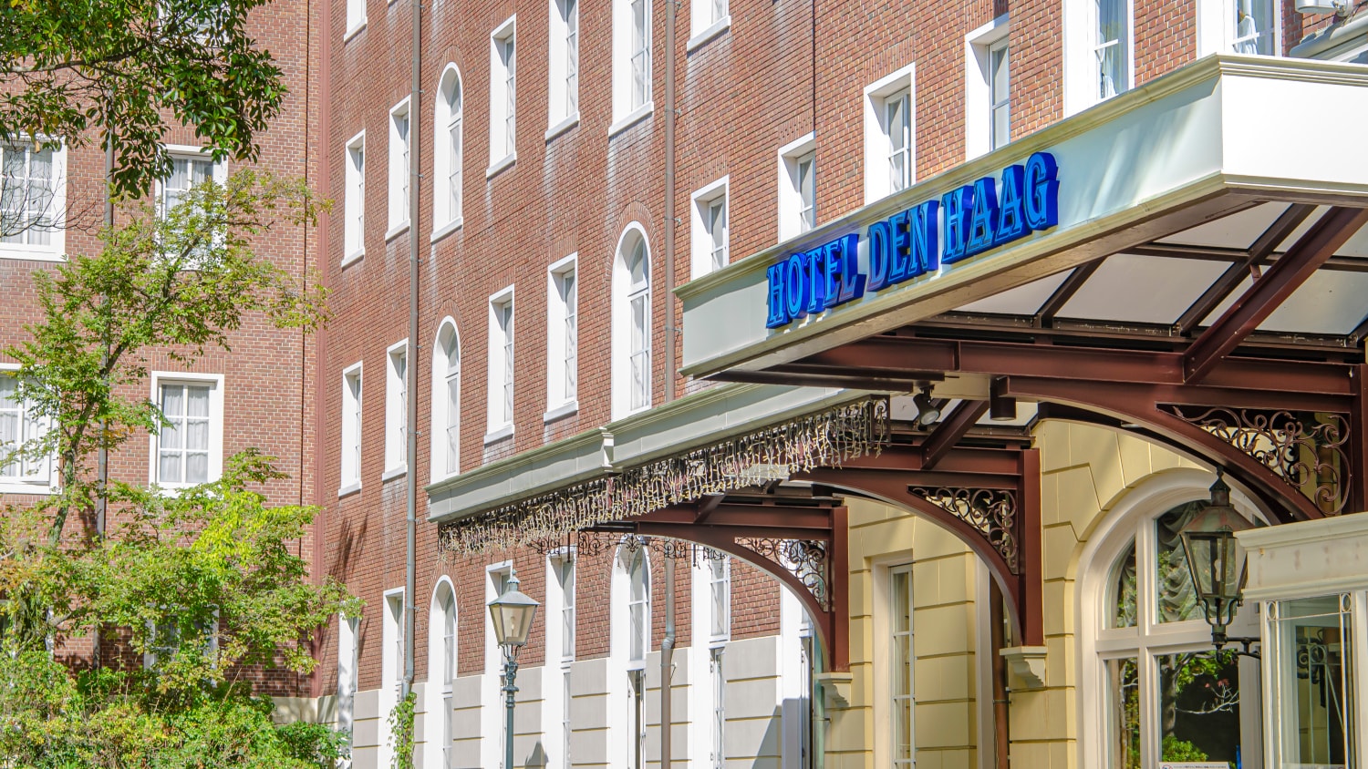 The hotel's forest-facing main entrance is bathed in sunlight filtering through the trees.